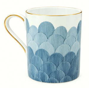 The Marie Daâge Cercle D’Ecailles Gold Filet by Marie Daâge is a white ceramic mug with a gold rim and handle, featuring a blue scallop pattern that wraps around the lower portion, inspired by classic French tableware.