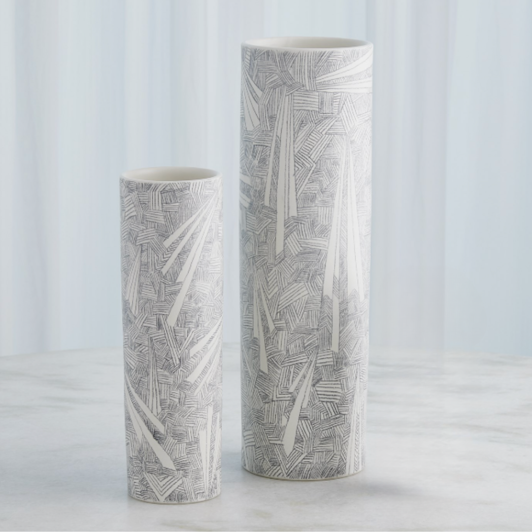 Two tall, cylindrical Searchlight Vases by Global Views/Surya with geometric black-and-white line patterns stand on a light gray surface against a softly blurred light blue background.