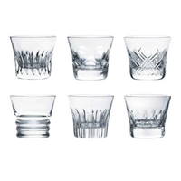 The Baccarat Everyday Tumblers Set of 6 features clear crystal glasses, each with a unique pattern, arranged elegantly—ideal for everyday use or gifting in a luxury box.