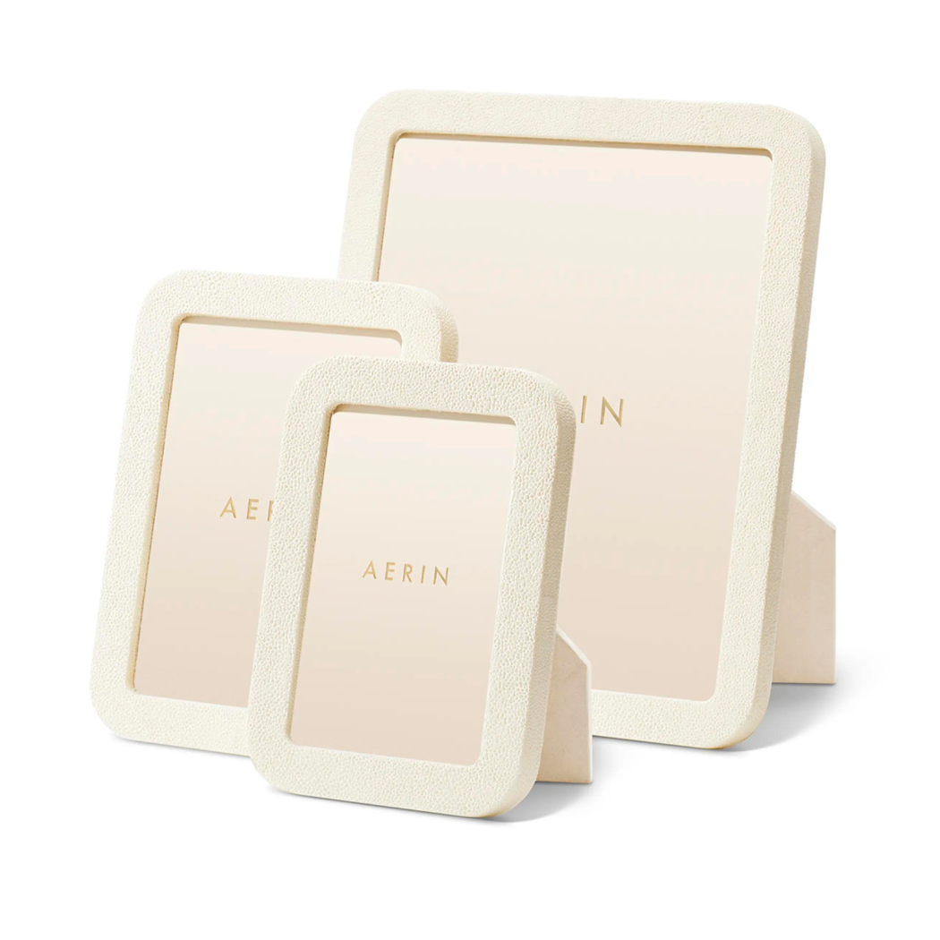 Three Modern Shagreen Frame Creams by Aerin, in various sizes, are shown upright with easel backs. Each features an ivory embossed texture and a beige insert with "AERIN" printed in gold at the center.