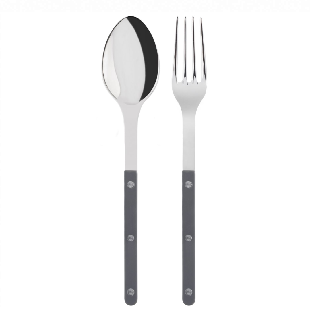 The Bistrot Shiny Solid Serving Set by Sabre features a metal spoon and fork with shiny silver heads and dark gray handles accented by three silver rivets, displayed side by side on a white background for a Parisian touch.