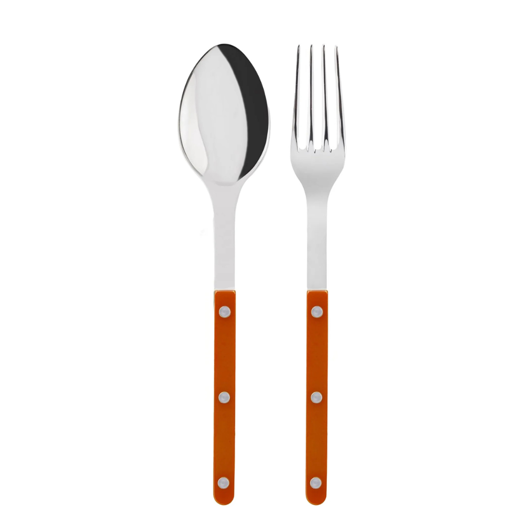 The Sabre Bistrot Shiny Solid Serving Set includes a metal spoon and fork with shiny silver heads and orange handles accented by three silver rivets, displayed side by side on a white background for Parisian style.