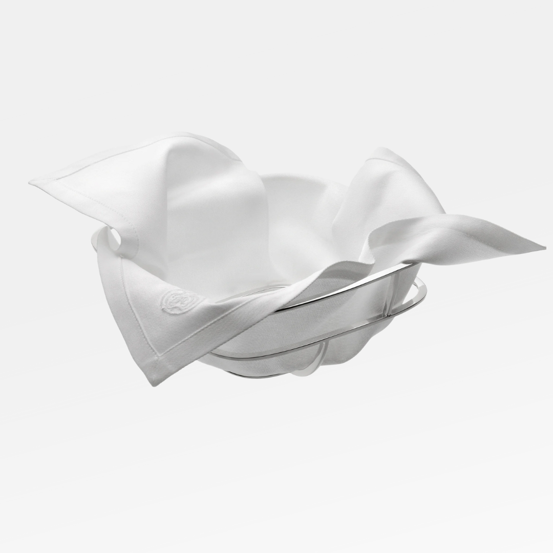 The Christofle Silver Time Bread Basket, lined with a white cloth napkin, is elegantly displayed against a plain white background.