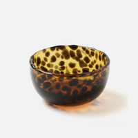 The Blue Pheasant Andrew Tortoise Nut Bowl is a small, round, hand-blown glass serving bowl featuring a glossy tortoiseshell pattern in amber, brown, and yellow tones against a plain white background.