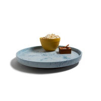 The Trashy Goods Smart Lazy Susan, a round light blue sustainable tray, holds a yellow bowl of popcorn and a small wooden container with spoon, all set on a white background.