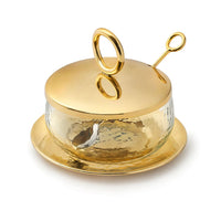 The Godinger Sphere Condiment Set Gold includes a round glass jar with a gold-toned hammered metal lid and matching spoon, both with circular handles, all resting on a gold-toned saucer for an elegant serving arrangement.