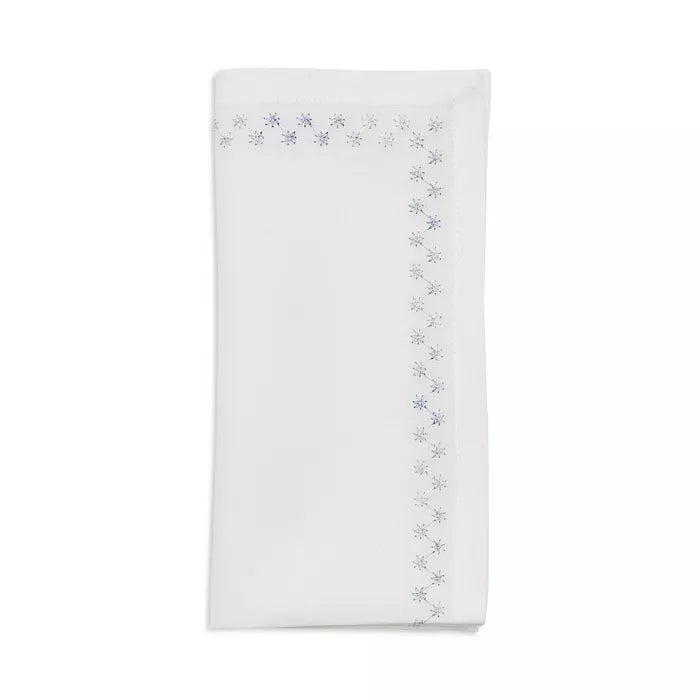 The Kim Seybert Starry Night Napkin Set of 4 in White & Blue features folded napkins with small light blue snowflake borders and delicate metallic embroidery along two edges.