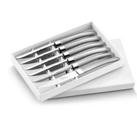 The Capdeco Le Thiers Steak Knives Matte Silver Set of 6 features stainless steel knives with curved handles, inspired by classic French design, elegantly arranged in a white presentation box with the lid partially open.