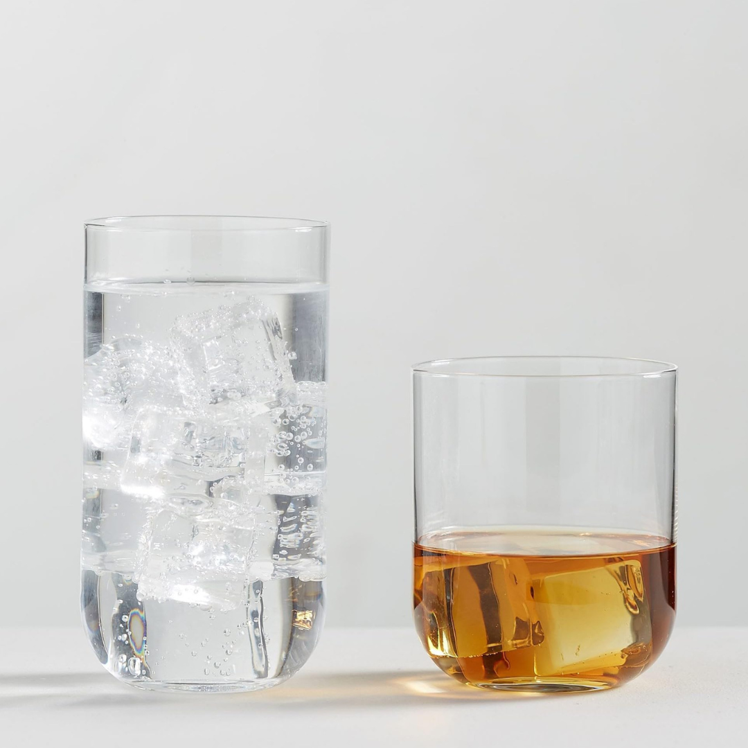 Two clear glasses from the Luigi Bormioli Sublime DOF Set of 4 rest on a light surface—one tall, filled with sparkling water and ice, and one short with an amber drink. Both are dishwasher safe for easy cleaning.