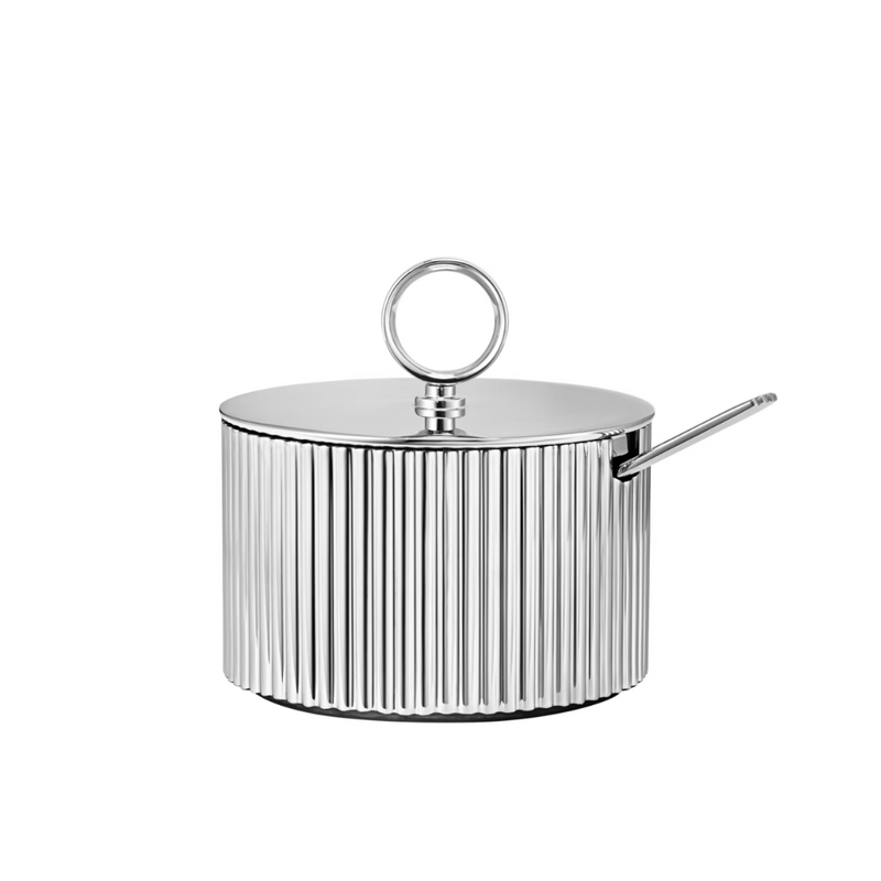 The Georg Jensen Bernadotte Sugar Bowl boasts a shiny stainless steel, ribbed body, round lid handle, and side spoon opening, embodying elegant Scandinavian design against a white background.