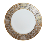 The Syracuse Dinnerware-Taupe by Haviland & Parlon features fine white porcelain with an ornate gold dotted rim forming concentric circles, offering elegance reminiscent of classic Limoges porcelain.