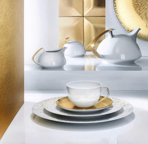 The Rosenthal Tac Skin Gold Dinnerware features elegant white porcelain with gold accents and durable glaze, including teacup, saucer, plates, teapot, creamer, and sugar bowl, displayed on a glossy white surface with gold decor.