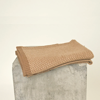 A folded Taiga Throw Gobi & Sand by Hangai Mountain Textiles rests on top of a gray concrete block against a plain, light background.