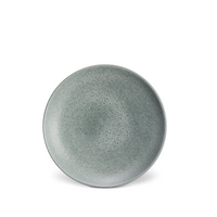 A round, gray ceramic plate with a speckled texture from above on a white background showcases the handcrafted Terra Seafoam Dinnerware by L'Objet, inspired by their signature artisanal style.