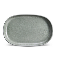 A large, oval-shaped ceramic plate from L'Objet’s Terra Seafoam Dinnerware, with a smooth, slightly speckled gray-green surface and rounded edges, shown from above on a white background.