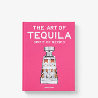 A bright pink hardcover copy of The Art of Tequila by Assouline, featuring an illustration of a decorative decanter that explores tequila history on its cover.