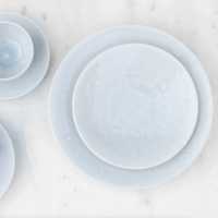 A top-down view of light blue Jars - Rosenthal Tourron Dinnerware - Opale stoneware plates and bowls stacked on a white marble surface.