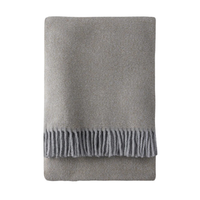 The Tweed Weave Throw by A Soft Idea is a neatly folded, light gray textured blanket with fringe detail along one edge, displayed on a white background.