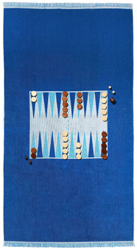 The G. McGee Southampton Beach Backgammon rug displays a central backgammon design in blue and white, with wooden game pieces arranged on the patterned section as if mid-game.