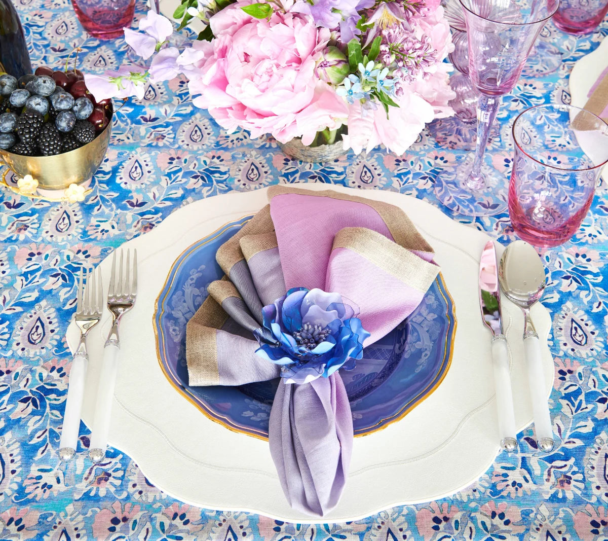 Create a beautiful table setting with layered blue and white plates arranged on the Kim Seybert Tailored Placemat s/4 in White. Add a gold-trimmed napkin ring to hold pink and purple napkins, topped with a blue flower for an elegant touch. Pink glasses, silverware, and a floral centerpiece complete this sophisticated look.