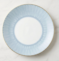 The Marie Daâge Ruban 1 Dinnerware by Marie Daâge is a round Limoges porcelain plate with a wide pale blue rim featuring subtle radial brushstrokes and a thin gold edge, set on light marble. The center remains plain white.