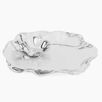 The Beatriz Ball Vento Bergamo Oven Platter & Bowl is a shiny, silver aluminum alloy serving piece with an irregular wavy edge and an attached small bowl with matching rim for dips or sauces.