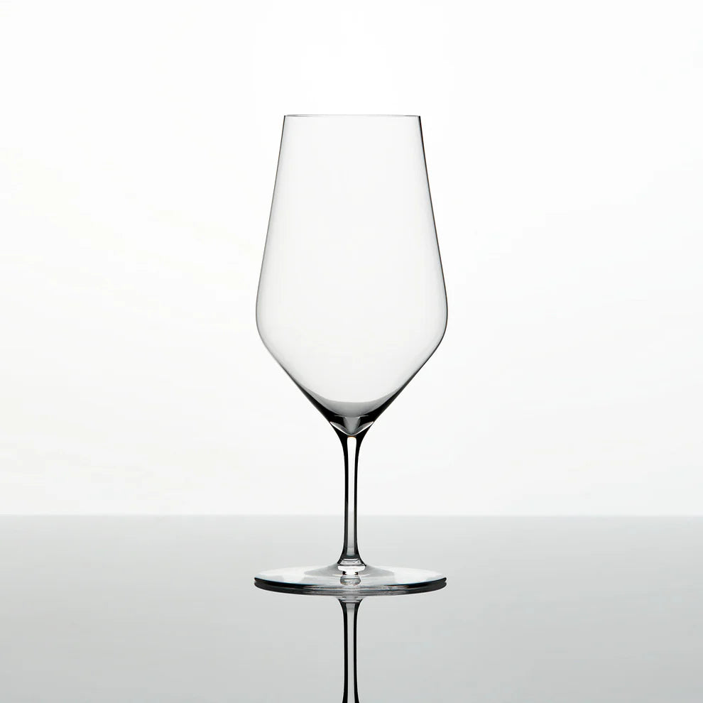 A single Zalto Water Glass by Grand Cru Selections / Zalto, featuring a thin stem and wide bowl, stands empty on a reflective surface against a plain white background.