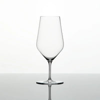 A single Zalto Water Glass by Grand Cru Selections / Zalto, featuring a thin stem and wide bowl, stands empty on a reflective surface against a plain white background.