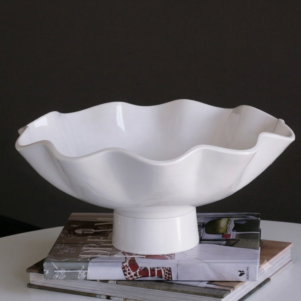 The Beatriz Ball Vida Havana Carola Pedestal Bowl White - Large sits atop stacked magazines on a white surface, forming an elegant dining centerpiece set against a dark background.