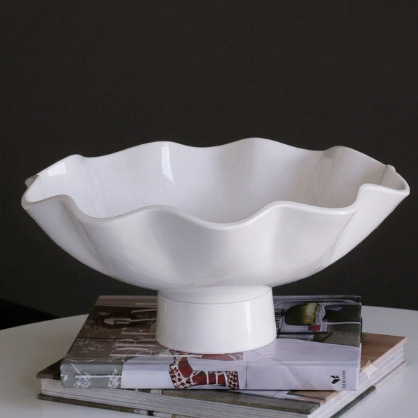 The Beatriz Ball Vida Havana Carola Pedestal Bowl White - Large sits atop stacked magazines on a white surface, forming an elegant dining centerpiece set against a dark background.