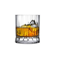 A clear Nude Glassware Wayne DOF glass from the Set of 4, featuring vertical ridges and crafted from lead-free crystal, is filled with amber whiskey and ice cubes, displayed against a plain white background.
