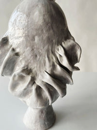 The Without Her Vase by Ellen Robinson Studio is a glossy, abstract ceramic sculpture with organic, flowing shapes and ruffled edges, finished in a sleek white glaze and displayed on a round base against a plain light background.