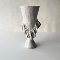 The Without Her Trumpet Vase by Ellen Robinson Studio features a textured, light gray hand-formed design with an abstract, sculpted leaf motif on the front, set against a plain, softly lit background.