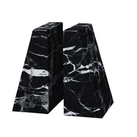 The Zeus Marble Bookend Set by Designs by Marble Crafter features two handcrafted black marble bookends with striking white veining, each shaped like a trapezoidal prism. Displayed side by side on a white background, these elegant accents elevate the decor of any room.
