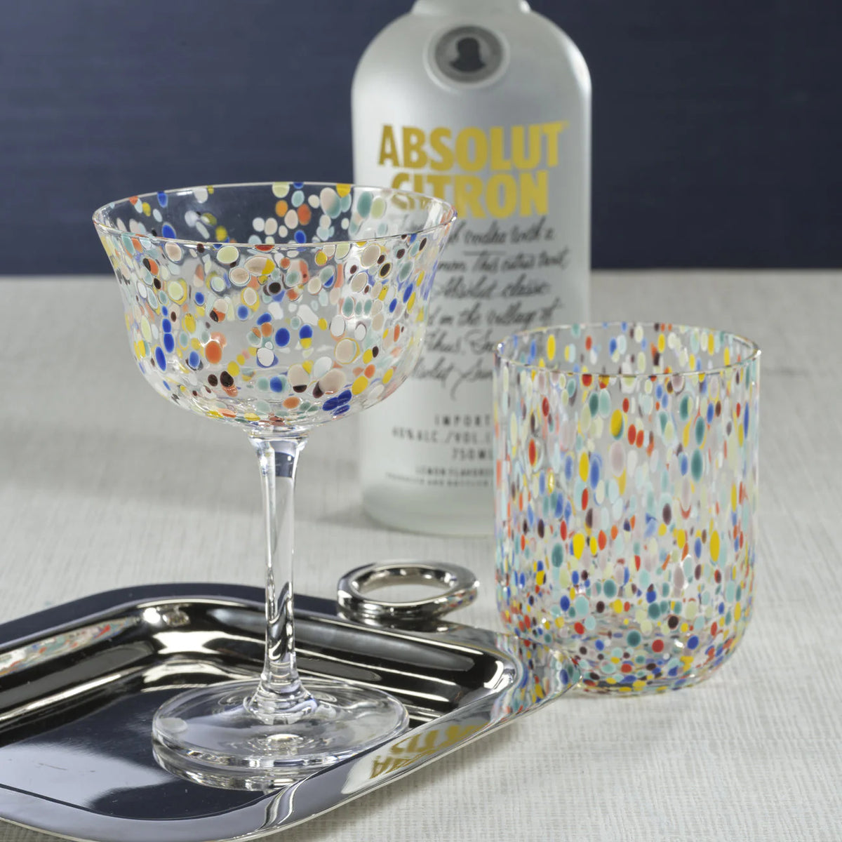 A Zodax Spritz Sprinkles Cocktail Glass sits on a tray beside a bottle of Absolut Citron, ready to brighten any festive table.