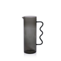 The Casa Smoke Pitcher by Zodax features a tall, cylindrical shape, narrow spout, and wavy handle. Its semi-transparent gray finish and modern design make it an eye-catching decor piece against any plain white backdrop.