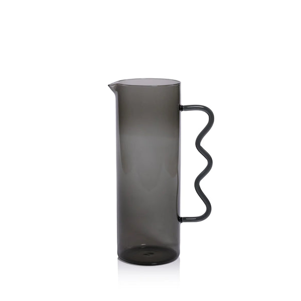The Casa Smoke Pitcher by Zodax features a tall, cylindrical shape, narrow spout, and wavy handle. Its semi-transparent gray finish and modern design make it an eye-catching decor piece against any plain white backdrop.