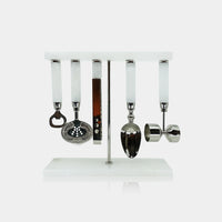 The Zodax Alabaster White Bar Tool Set features a sleek white stand that displays five stainless steel bar tools with alabaster white handles—a bottle opener, strainer, knife, spoon, and jigger—arranged neatly in a row against a minimalist backdrop. This set blends modern style with practical functionality, making it an ideal addition to any home bar.