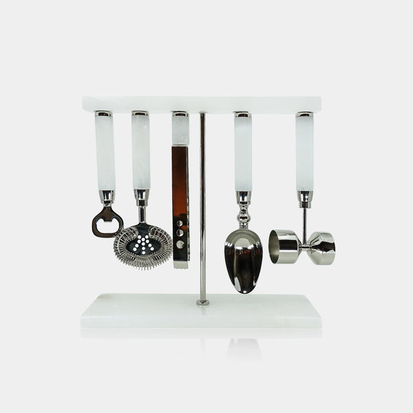 The Zodax Alabaster White Bar Tool Set features a sleek white stand that displays five stainless steel bar tools with alabaster white handles—a bottle opener, strainer, knife, spoon, and jigger—arranged neatly in a row against a minimalist backdrop. This set blends modern style with practical functionality, making it an ideal addition to any home bar.