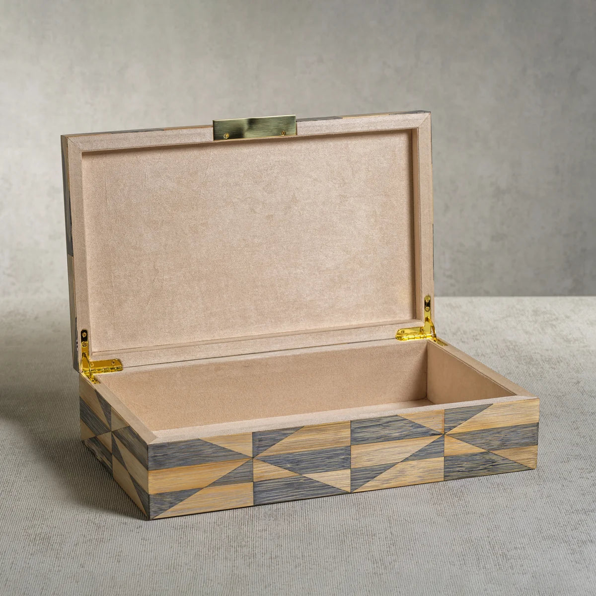 The Monarch Bamboo Box with Brass Trim by Zodax sits open on a neutral textured surface, displaying its plain, light-colored interior and polished gold hinges.