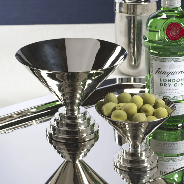 A silver martini glass, the Zodax Malcolm Condiment Bowl in polished nickel filled with green olives, a bottle of Tanqueray gin, and a cocktail shaker are arranged on a reflective tray in striking Art Deco style.