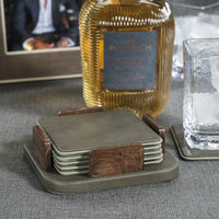 A Zodax Leather & Veneer Coaster Set - Cedar Green sits on the table beside a whiskey bottle, an empty glass with ice, and a framed photo in the background.