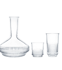 The Cadence Barware by Saint-Louis/Hermes features a clear glass decanter with ribbed detailing, accompanied by two hand-blown crystal tumblers with elegant ribbed bases.