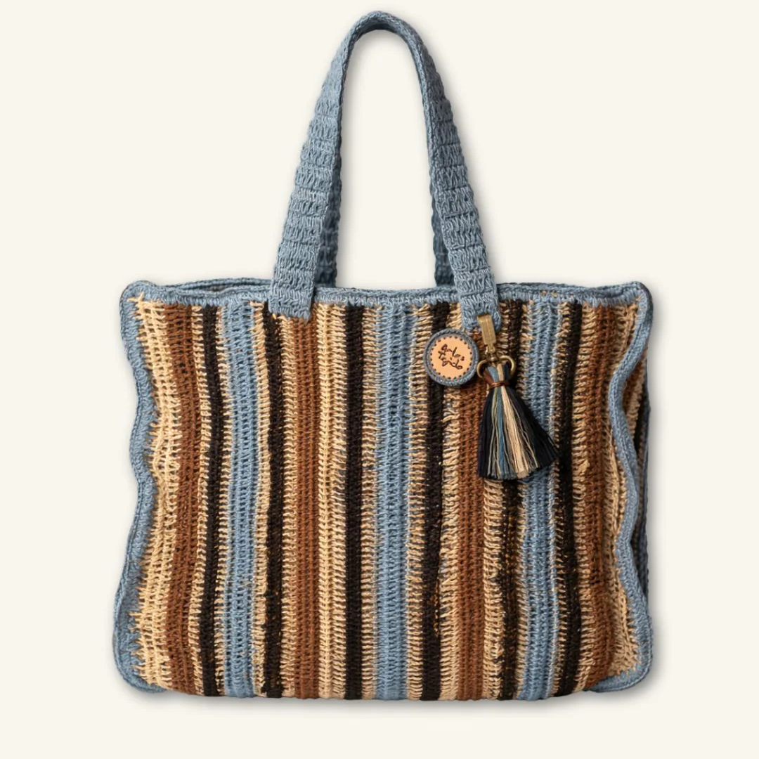 The Arte Striped Beach Tote - Blue by Arte & Tejido features vertical blue, beige, and brown stripes, two blue handles, a decorative tassel, and a round tag—perfect for adding bohemian flair to your summer outings.
