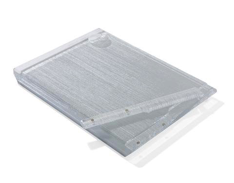 The Apeloig Collection Metallic Silver Acrylic Challah Board features a silver textured acrylic surface with a flat, transparent clip, styled as a modern challah board and displayed at an angle on a white background.