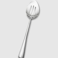 The Mary Jurek Alta Slotted Serving Spoon is featured on a light gray background, showcasing its textured handle and elegant, premium stainless steel design.