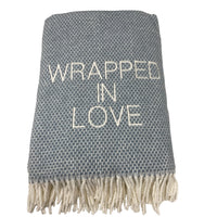 The A Soft Idea Wrapped in Love Throw is a super soft, gray woven blanket with white fringe and “WRAPPED IN LOVE” embroidered across the center. Machine washable, it makes the perfect holiday gift.