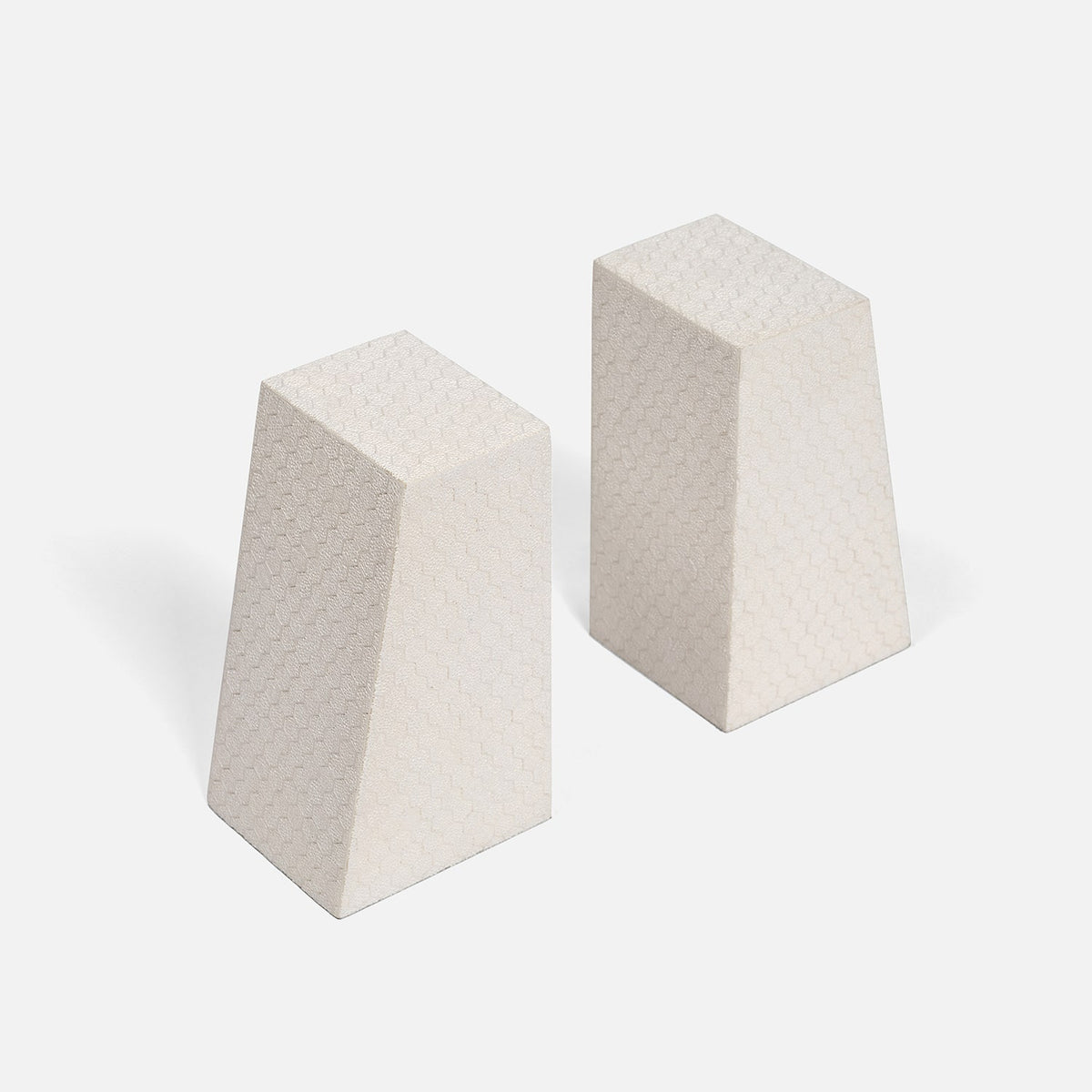 Two off-white, trapezoidal Rene Faux Shagreen Bookends by Made Goods, featuring subtle grid patterns and architectural edges, stand upright on a plain white background with light shadows cast to the left.