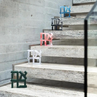 Five Ahava Sculptures by CDMX / BRUCI, in green, white, red, black, and blue, are arranged on the stone steps of a modern spiral staircase with concrete walls and a glass railing. The Ahava Sculpture is now back in stock.