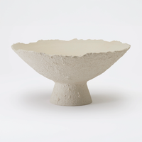 The Joelle Bowl by Dumae features a Sierra-textured, off-white finish with rough edges and a wide, shallow form. Its short cylindrical pedestal base highlights artisanal craftsmanship against a plain white background.